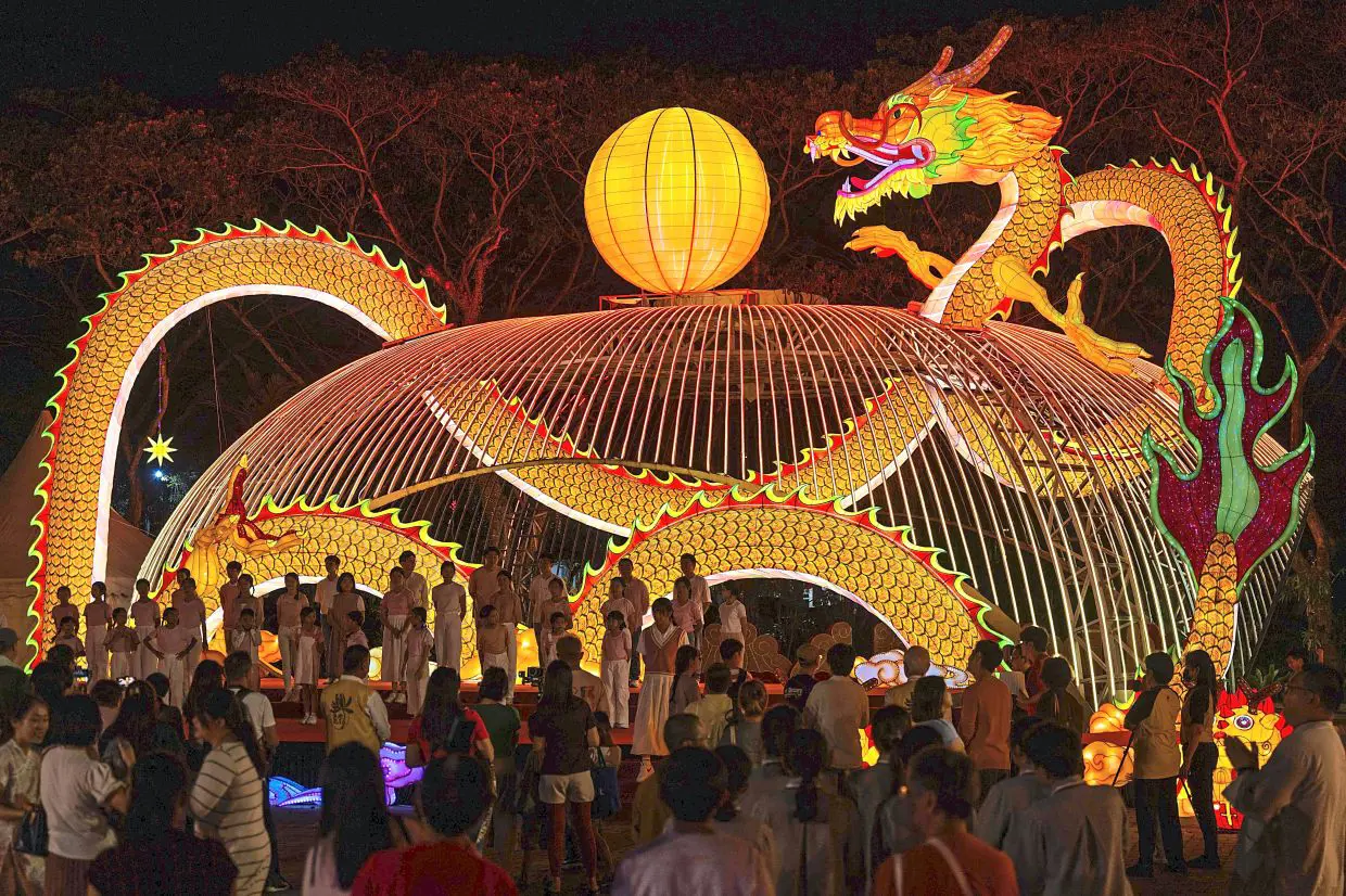 Illuminated dragon lantern sculpture at night surrounded by a crowd at a festival.